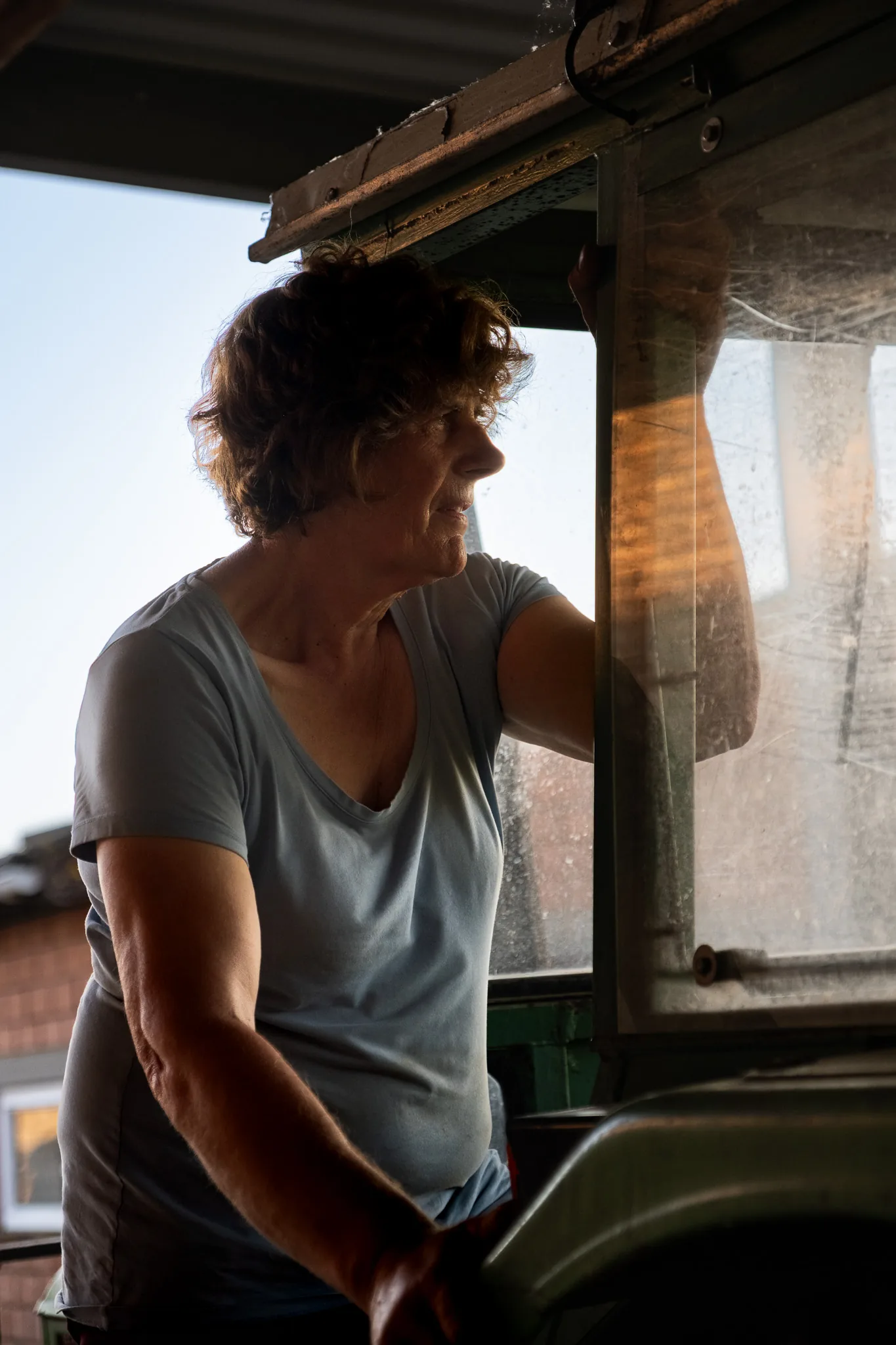 Boerin kijkt uit het raam van een groene tractor in warm avondlicht